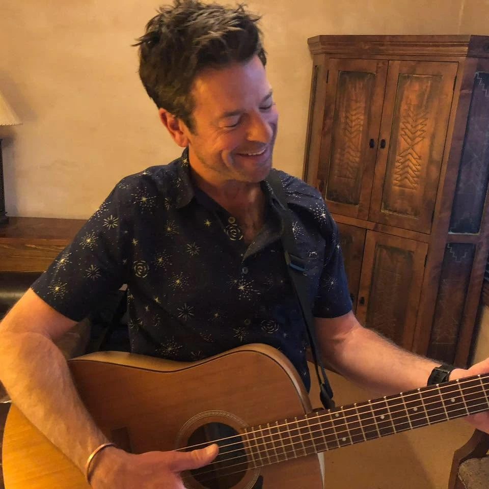 Joseph laughing as he plays an acoustic guitar, looking down at the strings.